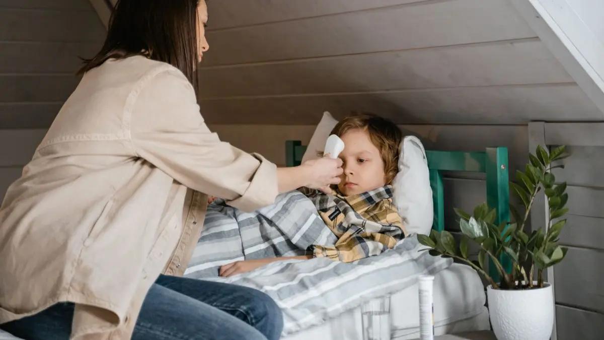 A parent checking a child's temperature with a thermometer at home