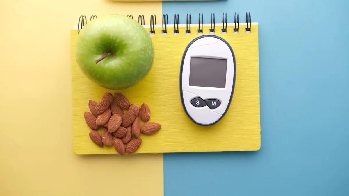 A blood glucose meter beside fresh fruit and nuts